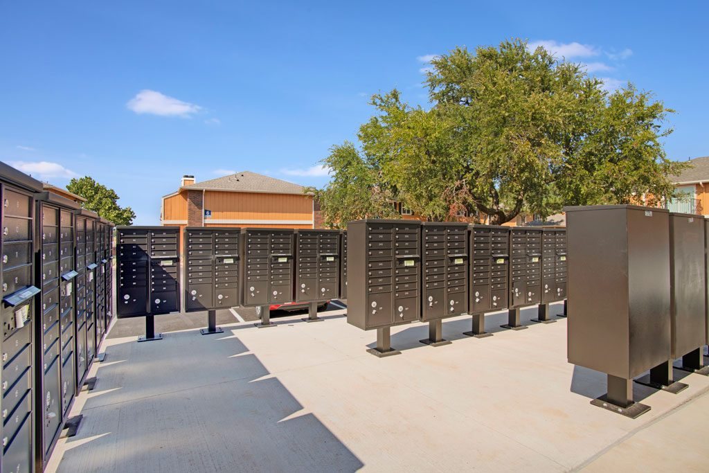 A series of tall, dark, metal lockers are lined up in a sunny courtyard.